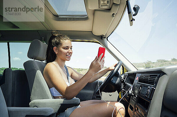 Lächelnde Frau checkt ihr Smartphone  während sie mit dem Wohnmobil fährt