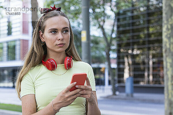 Junge Frau mit kabellosen Kopfhörern hält Smartphone in der Hand