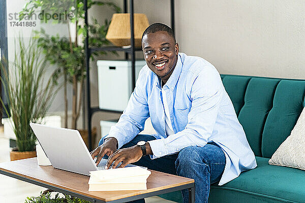 Glücklicher männlicher Profi mit Laptop  der zu Hause auf dem Sofa sitzt