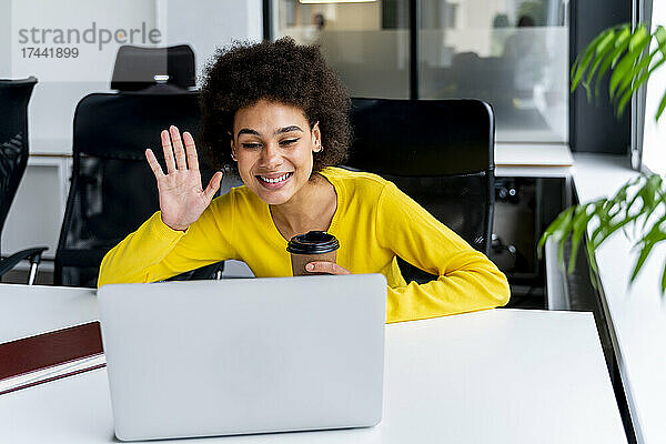Junge Geschäftsfrau winkt während eines Videoanrufs auf dem Laptop im Büro