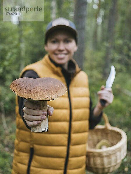 Lächelnde Frau zeigt Steinpilz im Wald