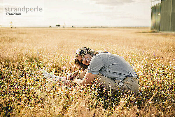 Frau lächelt  während sie ihre Knie auf einem landwirtschaftlichen Feld umarmt
