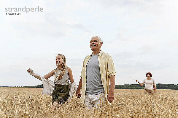 Enkelin hält Großvater beim Gehen auf dem Feld an den Händen