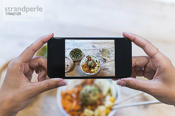 Frau fotografiert Essen mit Smartphone am Tisch