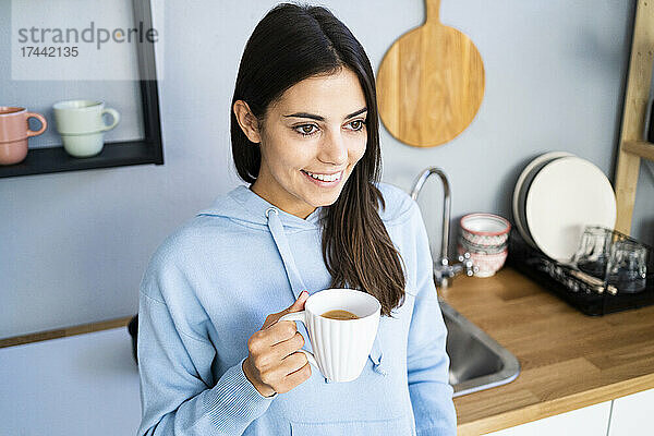 Schöne junge Frau hält Kaffeetasse in der heimischen Küche