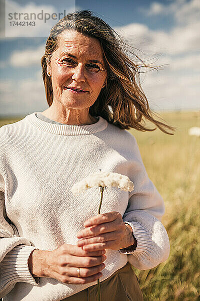 Lächelnde reife Frau mit Blume auf dem Feld