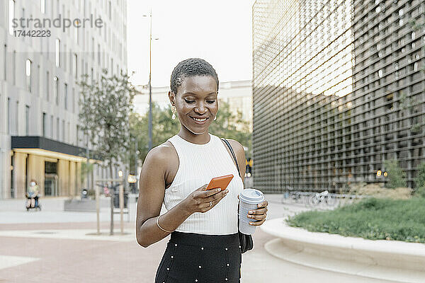 Geschäftsfrau mit Einwegkaffeetasse und Mobiltelefon in der Stadt