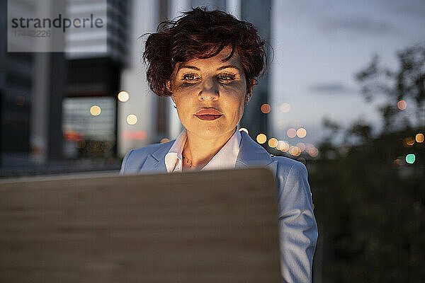 Schöne reife Geschäftsfrau  die in der Abenddämmerung einen Laptop benutzt