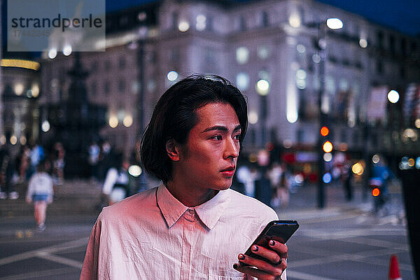 Hübscher Mann mit schwarzen Haaren  der sein Mobiltelefon in der Stadt hält