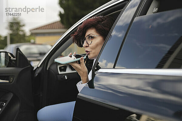 Reife Geschäftsfrau telefoniert über Lautsprecher  während sie im Auto sitzt