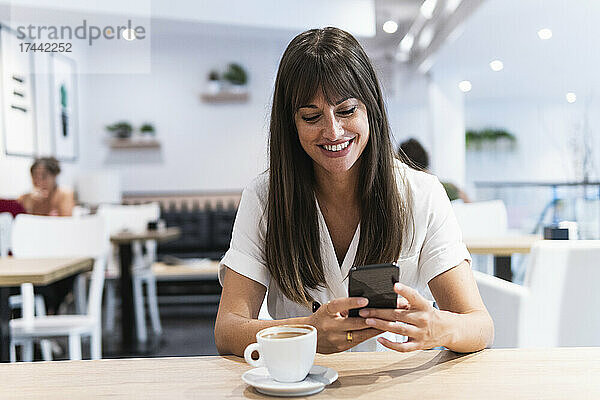 Lächelnde Geschäftsfrau mittleren Alters benutzt Smartphone im Restaurant