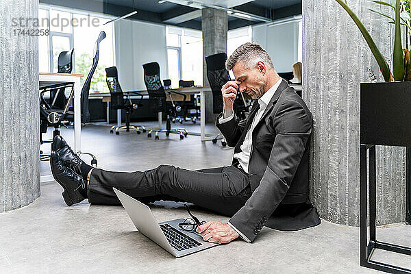 Müder Geschäftsmann mit Laptop sitzt auf dem Boden im Büro