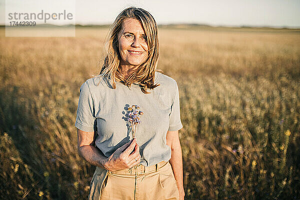 Lächelnde blonde Frau mit Blumenstrauß auf dem Feld
