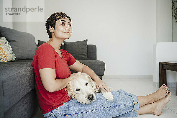 Nachdenkliche Frau mittleren Alters sitzt mit Golden Retriever zu Hause