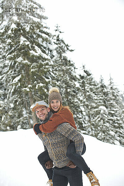 Lächelnder Mann mittleren Alters gibt einer Frau im Winter eine Huckepackfahrt