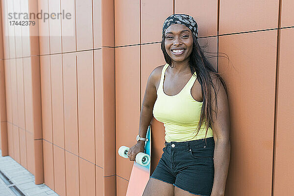 Glückliche Frau mit Skateboard  das an der Wand lehnt