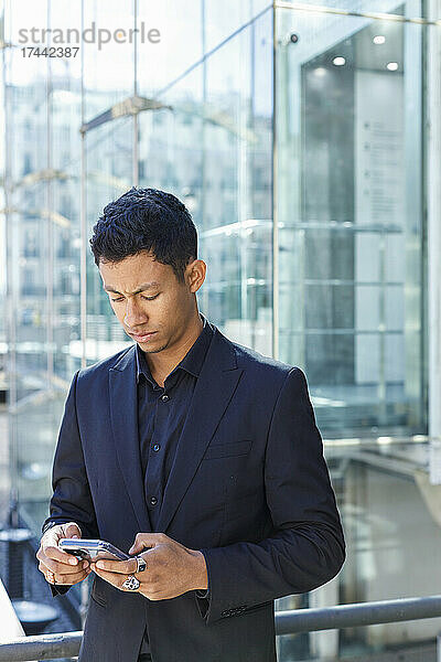 Junger Geschäftsmann schreibt Textnachrichten per Smartphone vor dem Bürogebäude