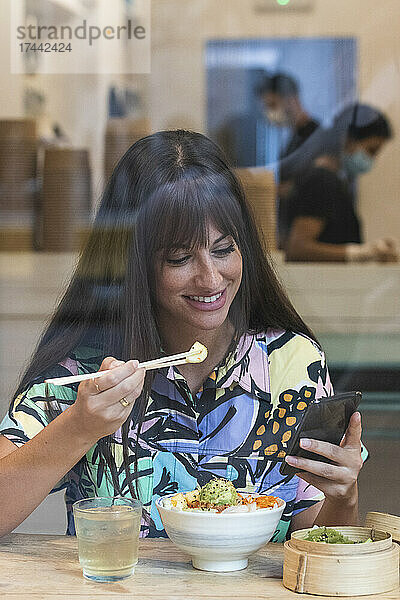 Frau benutzt Mobiltelefon beim Essen im Restaurant
