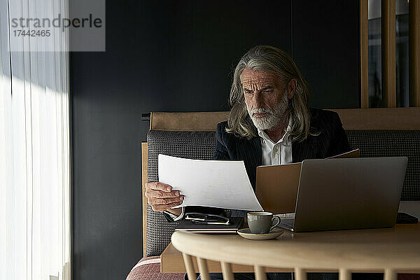 Männlicher Fachmann prüft Dokument  während er am Tisch im Hotelcafé sitzt