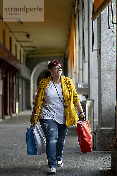 Lächelnde Frau mit Einkaufstüten  die am Flur läuft