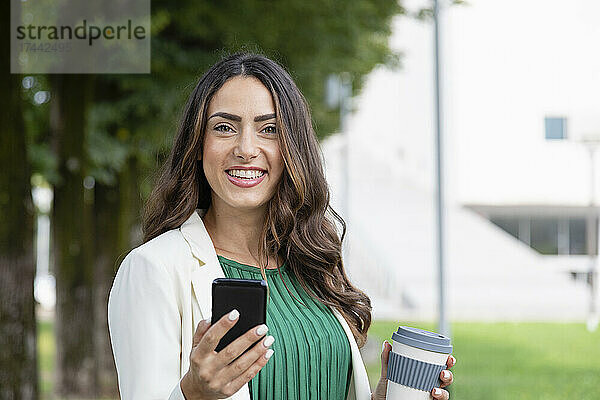 Glückliche junge Frau mit Mobiltelefon und Einwegkaffeetasse
