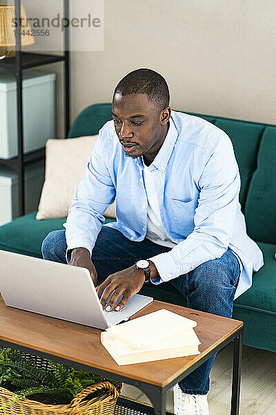 Männlicher Geschäftsmann benutzt Laptop  während er zu Hause auf dem Sofa sitzt