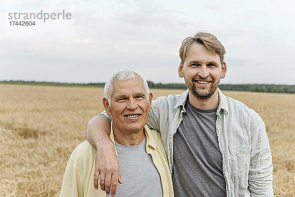 Lächelnder Sohn mit dem Arm um den älteren Vater auf dem Feld