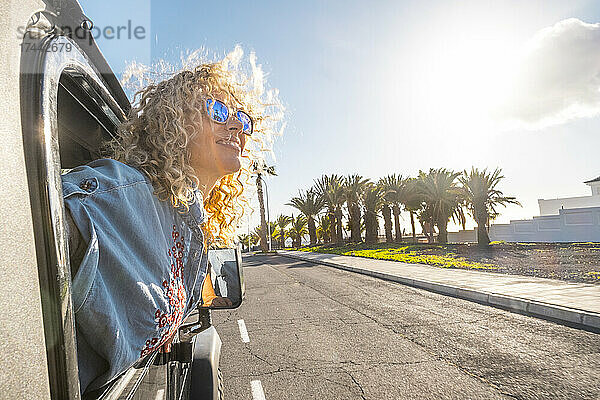 Lächelnde Frau lehnt an einem sonnigen Tag aus dem Autofenster