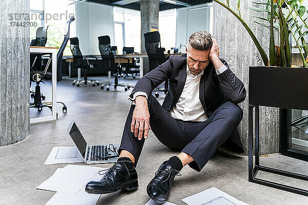 Geschäftsmann mit Kopf in der Hand sitzt auf dem Boden im Büro