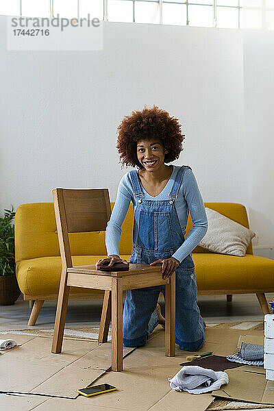 Lächelnde Afro-Frau poliert Holzstuhl im Wohnzimmer