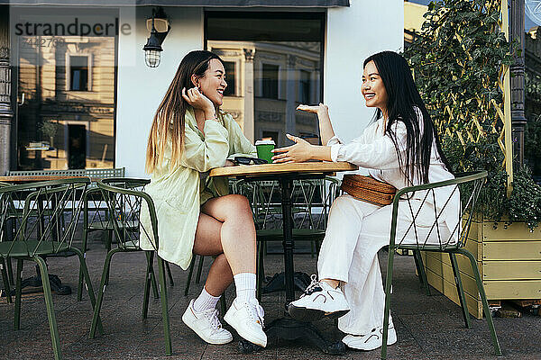 Lächelnde Freundinnen unterhalten sich im Straßencafé