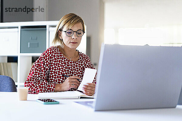 Mittlere erwachsene Frau  berufstätig  liest Papier am Schreibtisch