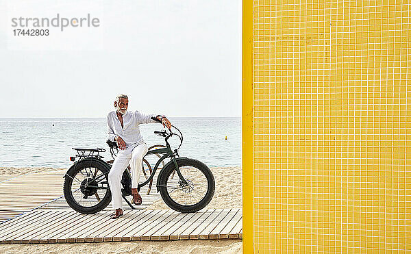 Reifer Mann sitzt auf dem Fahrrad am Strand