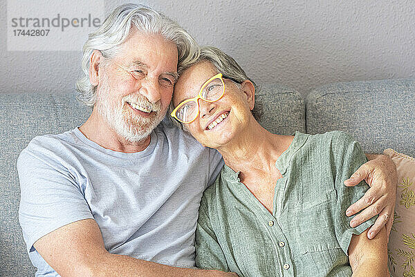 Lächelndes älteres Paar sitzt auf dem Sofa im Wohnzimmer