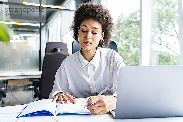 Geschäftsfrau schreibt Tagebuch  während sie mit Laptop am Schreibtisch sitzt