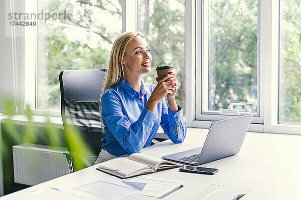 Blonde Geschäftsfrau trinkt Kaffee  während sie am Schreibtisch im Büro sitzt