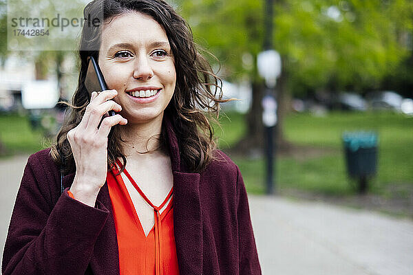 Lächelnde Frau  die im Park mit dem Handy telefoniert