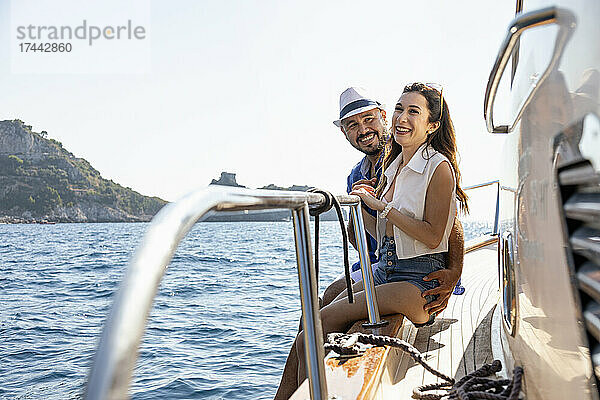 Lächelndes Paar sitzt an einem sonnigen Tag am Rand eines Motorboots