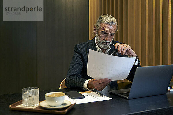 Reifer Geschäftsmann liest Dokument  während er am Schreibtisch sitzt