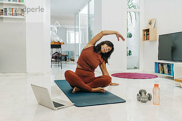 Aktive Frau praktiziert Yoga beim E-Learning per Laptop zu Hause