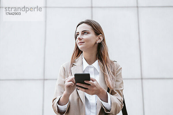 Geschäftsfrau hält Smartphone vor Wand