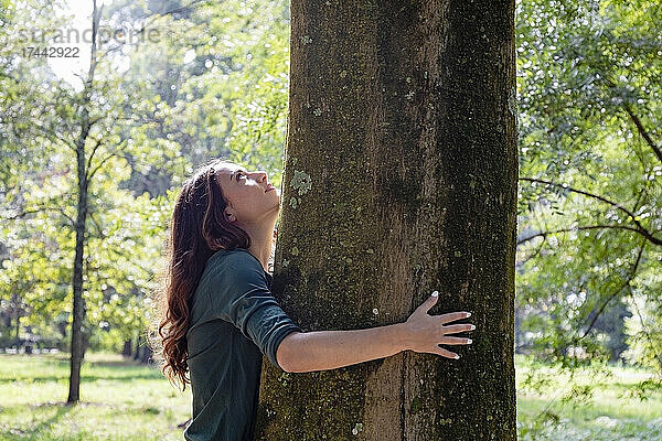 Frau umarmt sich  während sie Baum im Park betrachtet