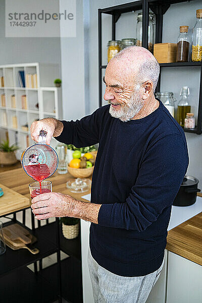 Älterer Mann gießt zu Hause Smoothie in Trinkglas