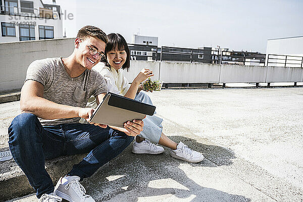 Lächelnde männliche und weibliche Freunde nutzen an einem sonnigen Tag ein digitales Tablet