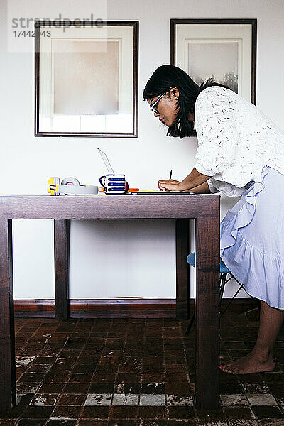 Freiberuflerin nutzt Laptop  während sie im Heimbüro am Schreibtisch steht