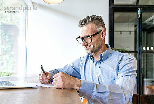 Männlicher Geschäftsprofi schreibt am Schreibtisch im Büro auf Papier