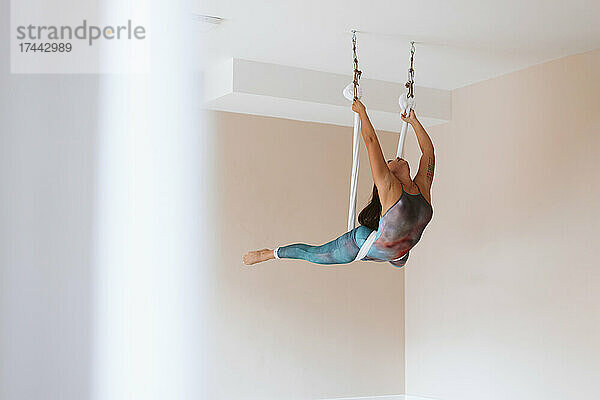 Sportlerin macht Dehnübungen  während sie im Studio Aerial Yoga praktiziert