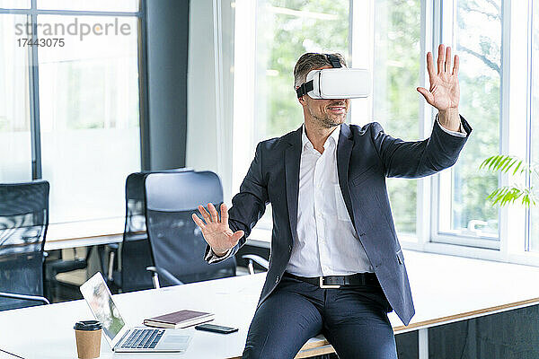 Geschäftsmann gestikuliert  während er im Büro ein Virtual-Reality-Headset trägt