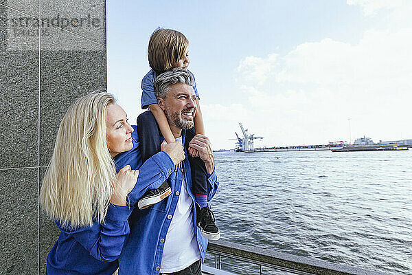 Lächelnde Familie blickt auf den Fluss  während sie am Geländer steht