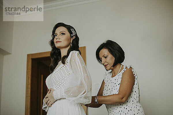 Mutter hilft Tochter beim Ankleiden für die Hochzeit zu Hause